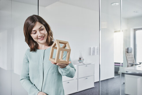 Lächelnde junge Geschäftsfrau, die ein Architekturmodell im Büro betrachtet - RORF01284