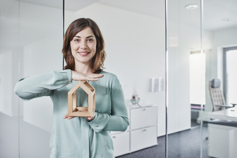 Porträt einer lächelnden jungen Geschäftsfrau, die ein Architekturmodell im Büro hält, lizenzfreies Stockfoto