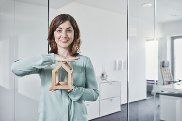 Porträt einer lächelnden jungen Geschäftsfrau, die ein Architekturmodell im Büro hält - RORF01285