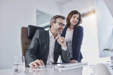 Smiling businessman and businesswoman looking at computer at desk in office - RORF01289