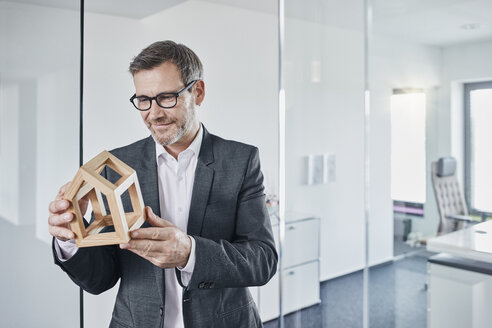 Lächelnder Geschäftsmann betrachtet ein Architekturmodell im Büro - RORF01291