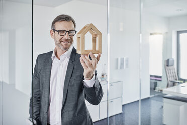 Lächelnder Geschäftsmann betrachtet ein Architekturmodell im Büro - RORF01294