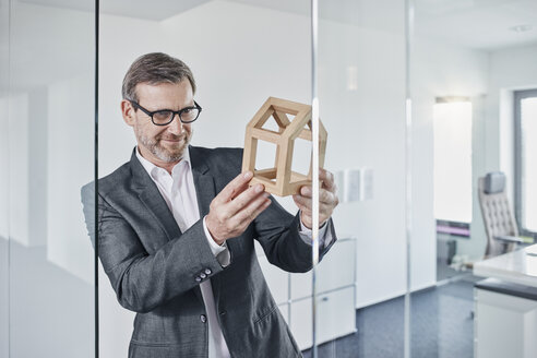 Lächelnder Geschäftsmann betrachtet ein Architekturmodell im Büro - RORF01296