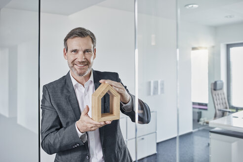 Porträt eines lächelnden Geschäftsmannes, der ein Architekturmodell im Büro hält - RORF01298