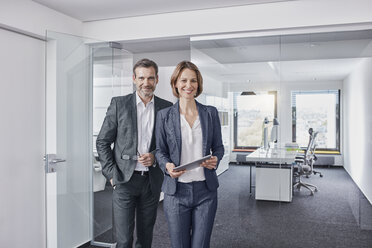 Portrait of smiling businessman and businesswoman with tablet in office - RORF01314