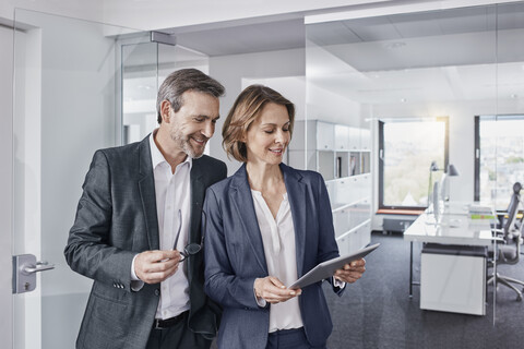 Lächelnder Geschäftsmann und Geschäftsfrau verwenden gemeinsam ein Tablet im Büro, lizenzfreies Stockfoto