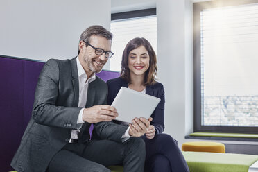 Smiling businessman and businesswoman using tablet in office lounge together - RORF01330