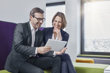 Smiling businessman and businesswoman using tablet in office lounge together - RORF01332