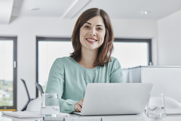 Portrait of smiling young businesswoman using laptop at desk in office - RORF01342