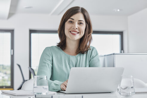 Porträt einer lächelnden jungen Geschäftsfrau mit Laptop am Schreibtisch im Büro - RORF01342