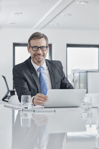 Portrait of smiling businessman with laptop at desk in office stock photo