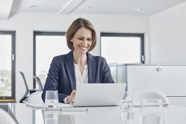 Smiling businesswoman using laptop at desk in office - RORF01349