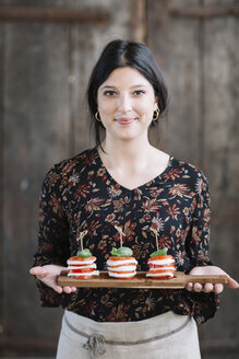 Porträt einer lächelnden Frau, die einen Caprese-Salat serviert - ALBF00534