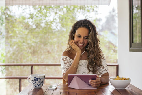 Woman using tablet and earphones at home - MOMF00451