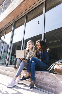 Friends sitting in front of window in the city, using laptop - UUF14146