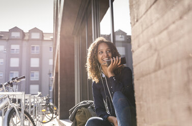 Junge Frau sitzt vor einem Fenster in der Stadt und benutzt ein Smartphone - UUF14151