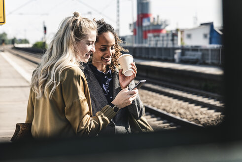 Freunde warten am Bahnhof und schauen auf ihr Smartphone - UUF14163