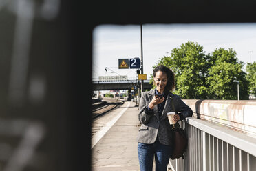 Junge Frau am Bahnhof liest Textnachrichten auf ihrem Handy - UUF14164