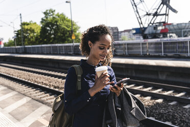 Young woman at train station reading text messages on her phone - UUF14165