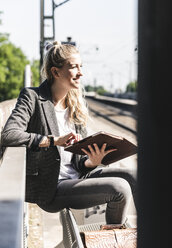 Junge Frau sitzt am Bahnhof und benutzt ein digitales Tablet - UUF14168
