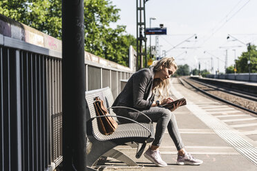 Junge Frau sitzt am Bahnhof und benutzt ein digitales Tablet - UUF14169