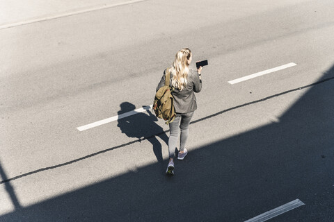 Junge Frau geht auf leerer Straße und spricht in ihr Smartphone, lizenzfreies Stockfoto