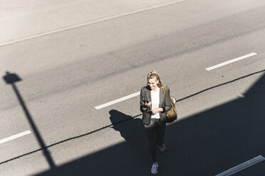 Young woman walking on empty road, talking into her smartphone - UUF14172