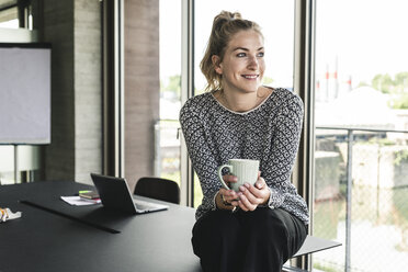 Junge Frau sitzt im Büro, macht eine Pause, trinkt Kaffee - UUF14179