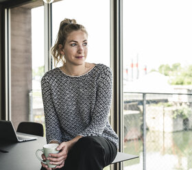 Junge Frau sitzt im Büro, macht eine Pause, trinkt Kaffee - UUF14181