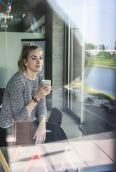 Junge Frau sitzt im Büro, macht eine Pause, trinkt Kaffee - UUF14183