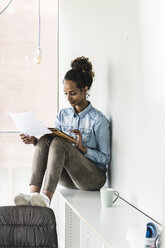 Young businesswoman sitting on shelf, using digital tablet, reading documents - UUF14188