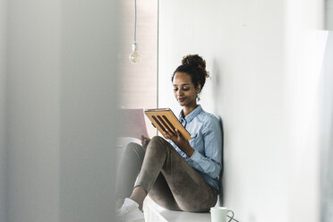 Young businesswoman sitting on shelf, using digital tablet - UUF14189