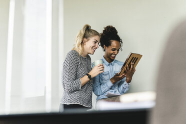 Kollegen arbeiten im Büro, schauen auf ein digitales Tablet, lachen - UUF14191