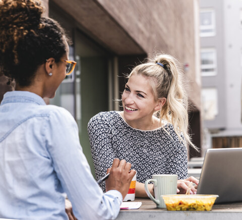 Young colleagues sitting outdoors, working together, having lunch stock photo