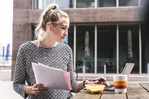 Junge Geschäftsfrau sitzt im Freien, arbeitet und isst zu Mittag - UUF14199