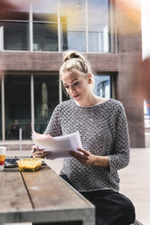 Junge Geschäftsfrau sitzt im Freien, arbeitet und isst zu Mittag - UUF14200