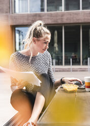 Young buisinesswoman sitting outdoors, working and having lunch - UUF14201