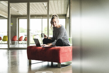 junge Geschäftsfrau arbeitet in einem modernen Büro, sitzt auf einem Hocker und benutzt einen Laptop - UUF14205