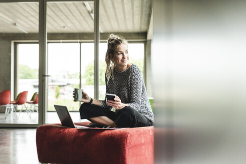 young businesswoman working in modern office, sitting on stool, using laptop - UUF14206