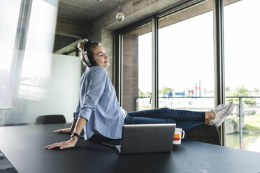 Young businesswoman sitting on desk, listening music - UUF14225