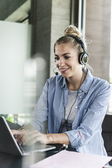 Young businesswoman sitting at desk, making a call, using headset and laptop - UUF14230