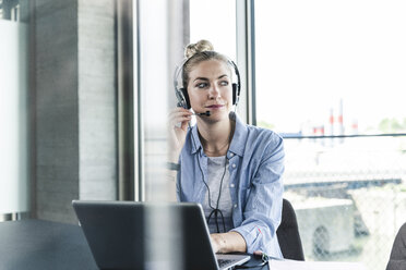 Junge Geschäftsfrau am Schreibtisch sitzend, telefonierend, mit Headset und Laptop - UUF14232