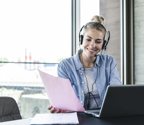 Junge Geschäftsfrau am Schreibtisch sitzend, telefonierend, mit Headset und Laptop - UUF14233