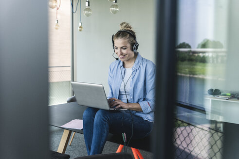 Young businesswoman sitting at desk, making a call, using headset and laptop - UUF14234