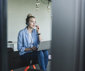 Junge Geschäftsfrau am Schreibtisch sitzend, telefonierend, mit Headset und Laptop - UUF14235