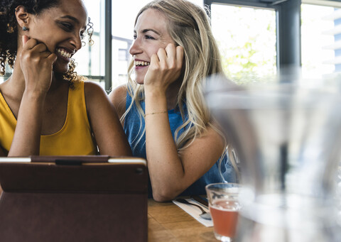 Beste Freunde treffen sich in einem Café, unterhalten sich und tauschen Neuigkeiten aus, benutzen ein digitales Tablet, lizenzfreies Stockfoto