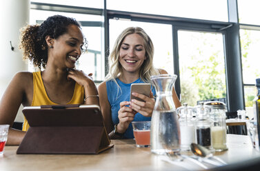 Beste Freunde treffen sich in einem Café, unterhalten sich und tauschen Neuigkeiten aus, benutzen ein digitales Tablet - UUF14243