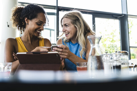 Beste Freunde treffen sich in einem Café, unterhalten sich und tauschen Neuigkeiten aus, benutzen ein digitales Tablet, lizenzfreies Stockfoto