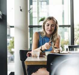 Junge Frau in einem Café, die Kaffee trinkt und Süßigkeiten isst - UUF14248