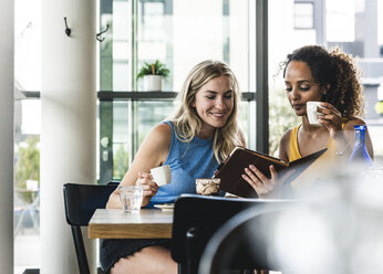 Beste Freunde treffen sich in einem Café, unterhalten sich und tauschen Neuigkeiten aus, benutzen ein digitales Tablet - UUF14250